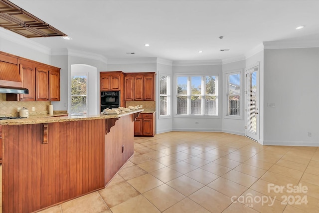 kitchen featuring tasteful backsplash, black double oven, kitchen peninsula, ornamental molding, and a kitchen breakfast bar