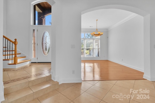 entryway with ornamental molding, light wood-type flooring, and an inviting chandelier