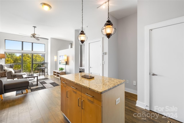 kitchen featuring light stone countertops, ceiling fan, a center island, dark hardwood / wood-style floors, and pendant lighting