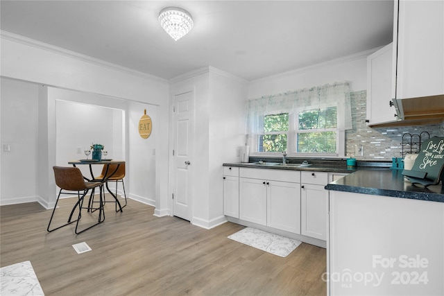 kitchen featuring sink, light hardwood / wood-style floors, white cabinets, crown molding, and decorative backsplash