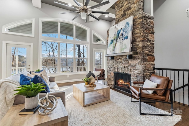 living room with a high ceiling, a stone fireplace, hardwood / wood-style floors, and ceiling fan