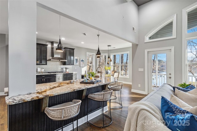 kitchen with dark hardwood / wood-style floors, decorative light fixtures, tasteful backsplash, a kitchen bar, and wall chimney range hood