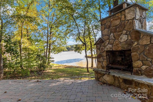 view of patio featuring a water view and an outdoor stone fireplace