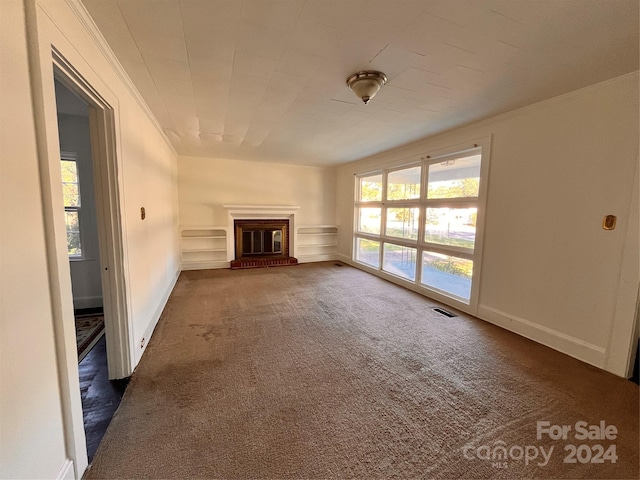 unfurnished living room with a brick fireplace, crown molding, and dark colored carpet