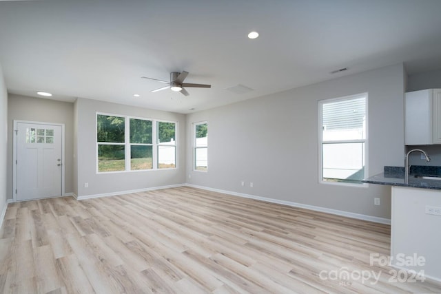 unfurnished living room featuring sink, light wood-type flooring, and ceiling fan