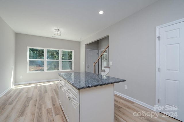 kitchen featuring white cabinets, light wood-type flooring, dark stone counters, and a center island