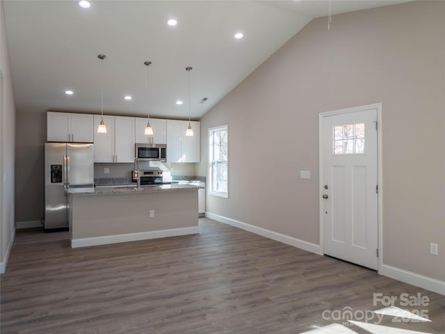 kitchen featuring white cabinetry, hanging light fixtures, a kitchen island with sink, stainless steel appliances, and light stone countertops