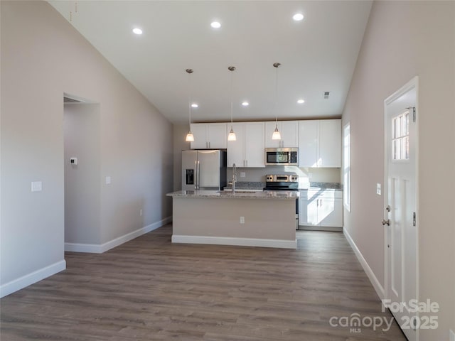 kitchen with appliances with stainless steel finishes, light stone countertops, an island with sink, white cabinets, and decorative light fixtures