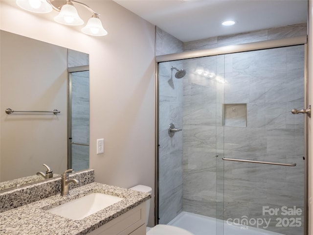 bathroom featuring a shower with door, vanity, and toilet