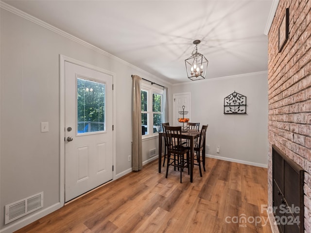 dining area with wood-type flooring, a notable chandelier, a fireplace, and ornamental molding