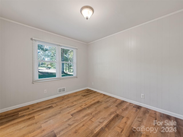 spare room featuring hardwood / wood-style flooring, crown molding, and wood walls