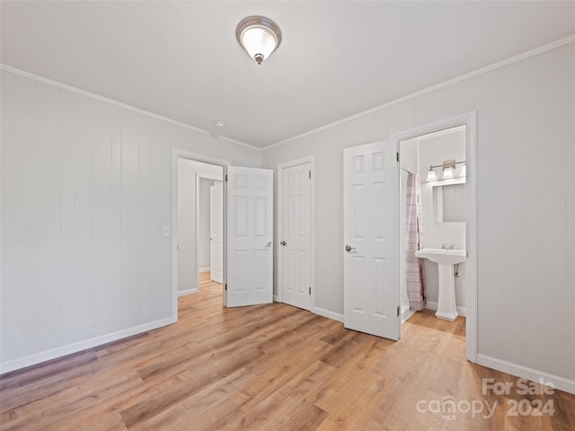 unfurnished bedroom featuring light wood-type flooring, sink, wooden walls, ornamental molding, and connected bathroom