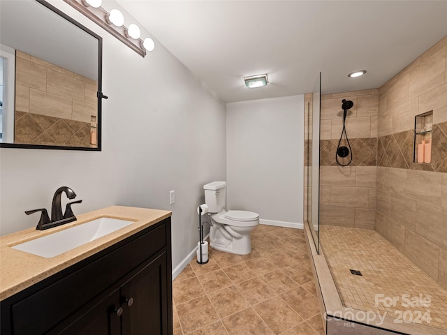 bathroom with tile patterned flooring, toilet, tiled shower, and vanity