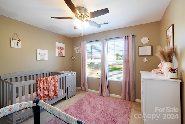 bedroom featuring ceiling fan, a crib, and light colored carpet