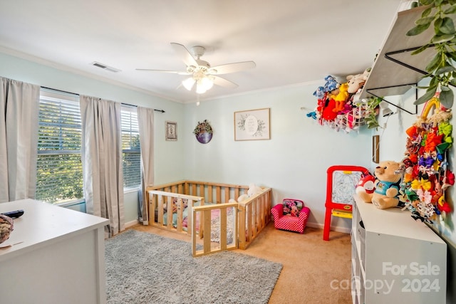 bedroom with a nursery area, light carpet, ornamental molding, and ceiling fan