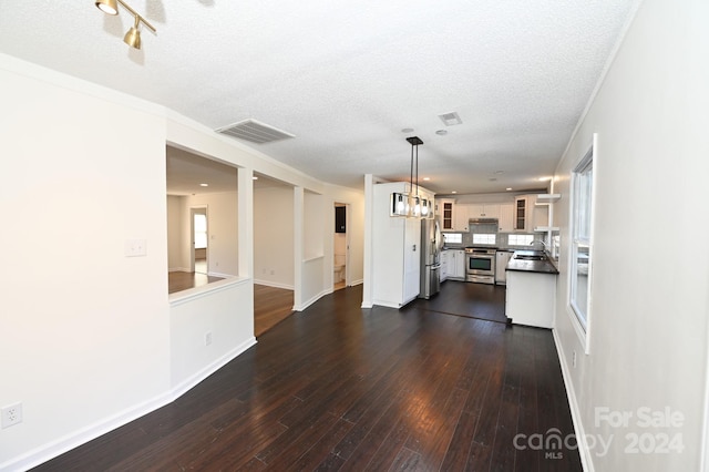 kitchen with dark wood-type flooring, white cabinetry, appliances with stainless steel finishes, decorative light fixtures, and a textured ceiling