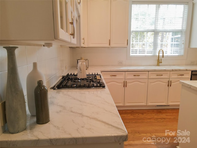 kitchen with sink, stainless steel gas cooktop, backsplash, white cabinets, and light wood-type flooring