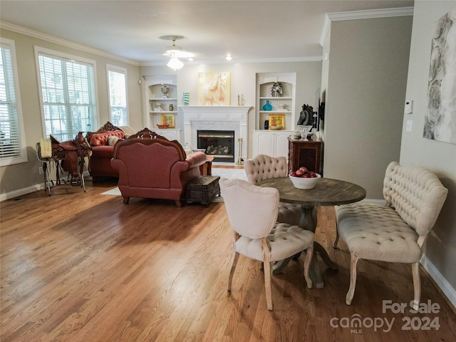 dining room featuring built in shelves, light hardwood / wood-style floors, crown molding, and a fireplace