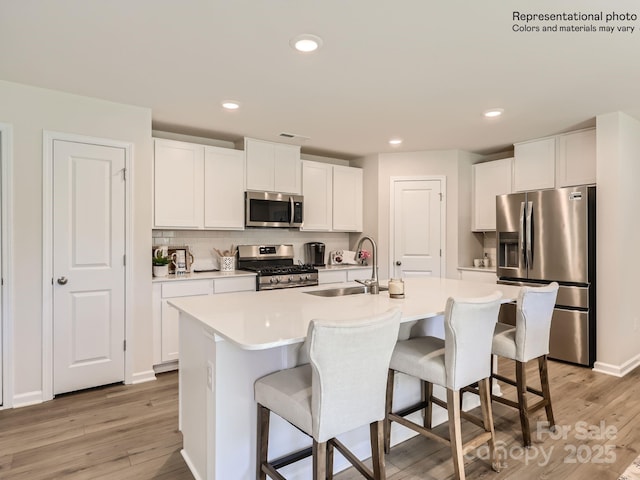 kitchen with sink, white cabinetry, stainless steel appliances, and a kitchen island with sink