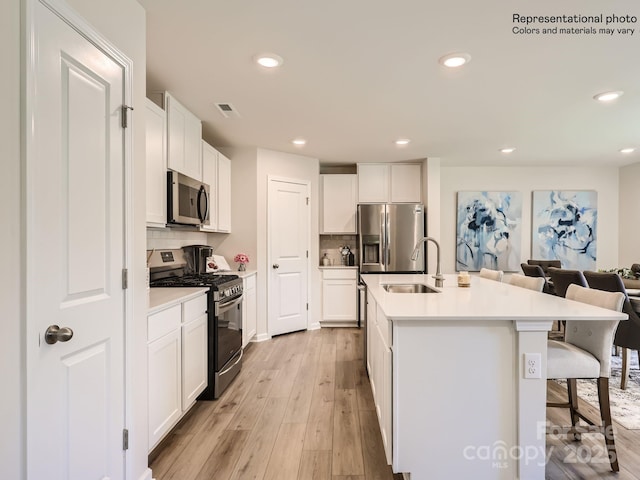 kitchen featuring an island with sink, appliances with stainless steel finishes, a kitchen breakfast bar, white cabinets, and sink