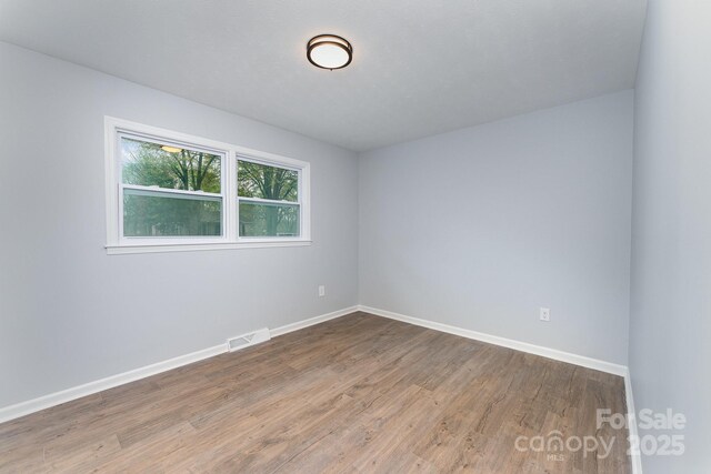 empty room featuring baseboards, visible vents, and wood finished floors