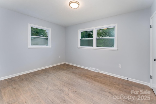 unfurnished room featuring plenty of natural light, visible vents, wood finished floors, and baseboards