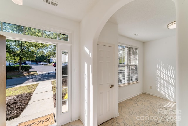 foyer entrance featuring visible vents, arched walkways, and baseboards