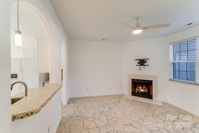 unfurnished living room featuring visible vents, a ceiling fan, a high end fireplace, arched walkways, and baseboards