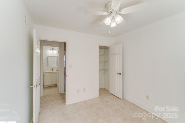 unfurnished bedroom with a spacious closet, baseboards, ceiling fan, and a sink