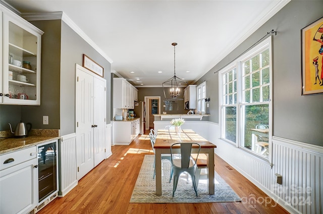 dining room featuring an inviting chandelier, beverage cooler, crown molding, and light hardwood / wood-style flooring