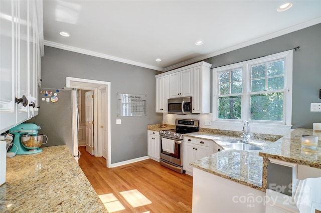 kitchen with light stone counters, white cabinets, sink, light hardwood / wood-style floors, and appliances with stainless steel finishes