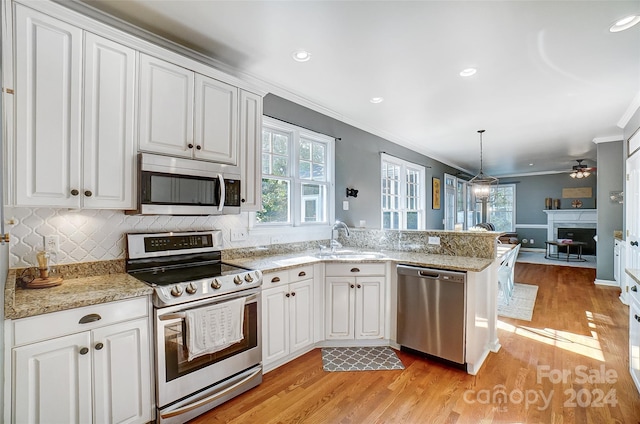 kitchen featuring pendant lighting, sink, kitchen peninsula, stainless steel appliances, and light hardwood / wood-style floors