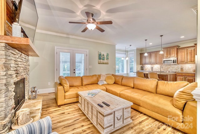 living room with light wood-type flooring, a fireplace, ceiling fan, and crown molding