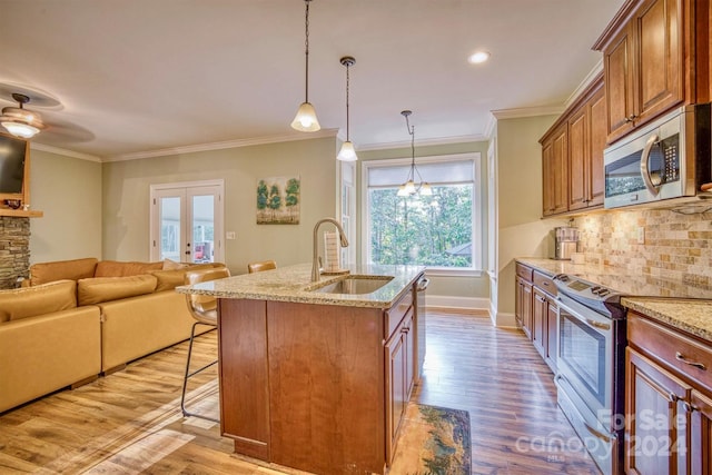 kitchen with a kitchen island with sink, light wood-type flooring, pendant lighting, sink, and stainless steel appliances