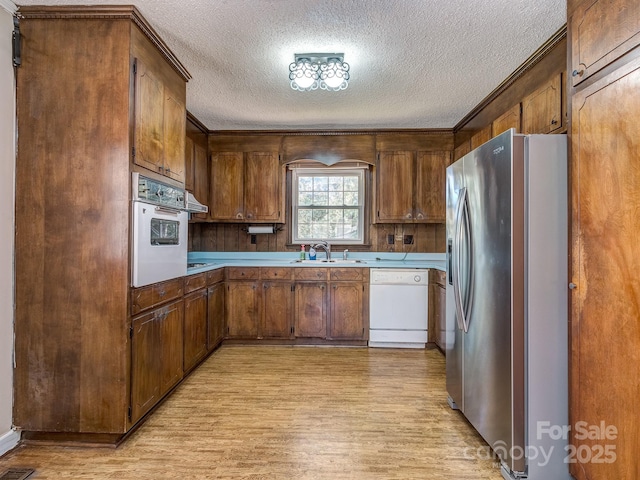 kitchen featuring a textured ceiling, light wood-type flooring, white appliances, and sink