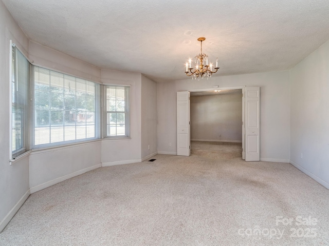 carpeted spare room featuring a chandelier and a textured ceiling