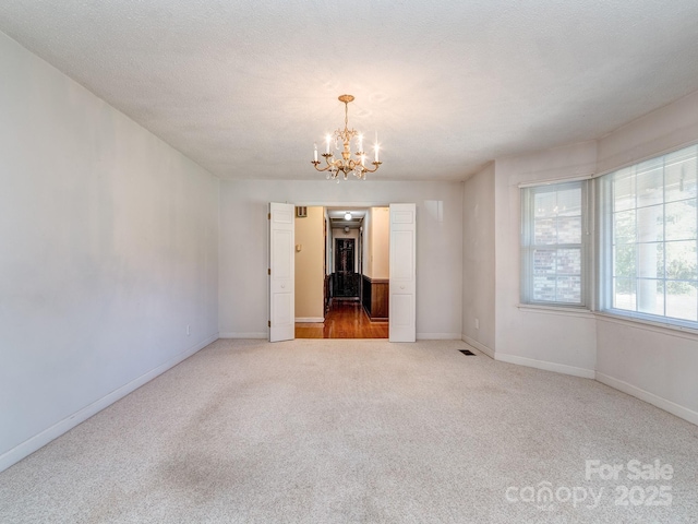 spare room featuring carpet, a textured ceiling, and an inviting chandelier