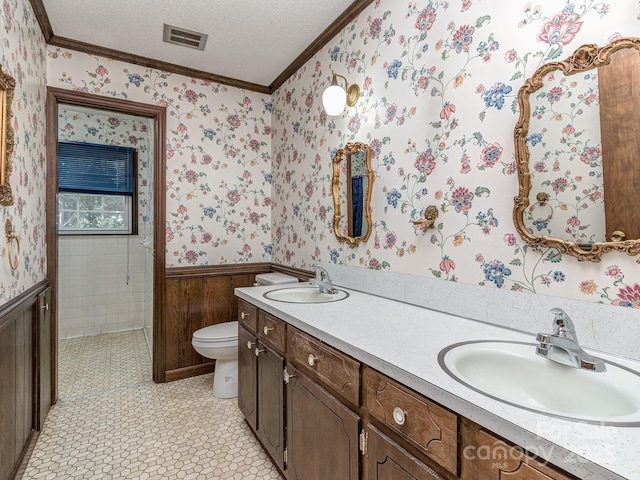 bathroom featuring vanity, wood walls, toilet, ornamental molding, and a textured ceiling