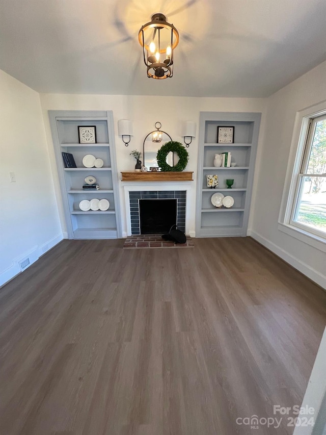 unfurnished living room featuring wood-type flooring, a notable chandelier, a brick fireplace, and built in shelves