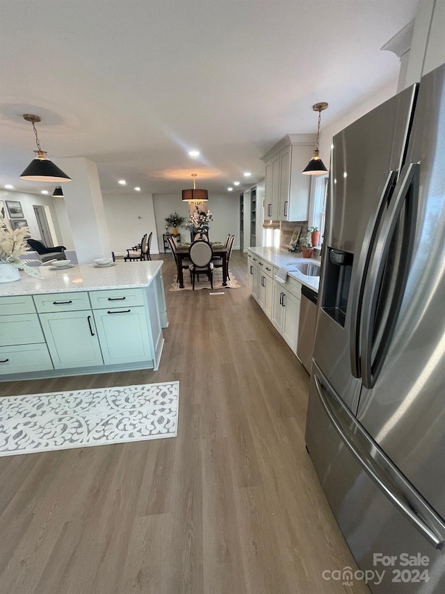 kitchen with wood-type flooring, white cabinets, pendant lighting, appliances with stainless steel finishes, and backsplash