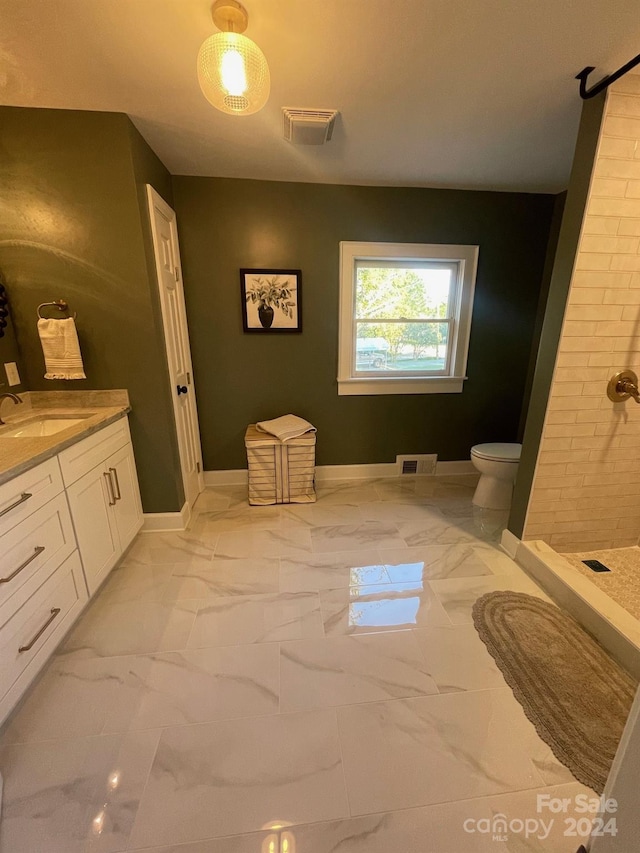 bathroom with toilet, tiled shower, and vanity