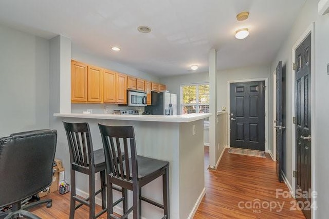 kitchen featuring light brown cabinets, a breakfast bar, light hardwood / wood-style floors, kitchen peninsula, and appliances with stainless steel finishes