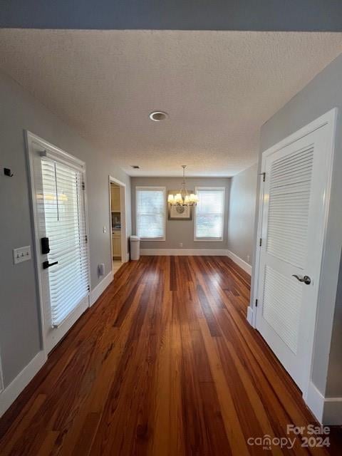 hallway with an inviting chandelier, a textured ceiling, and dark wood-type flooring