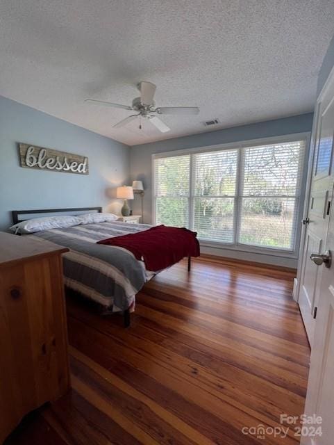 bedroom with ceiling fan, a textured ceiling, multiple windows, and hardwood / wood-style floors