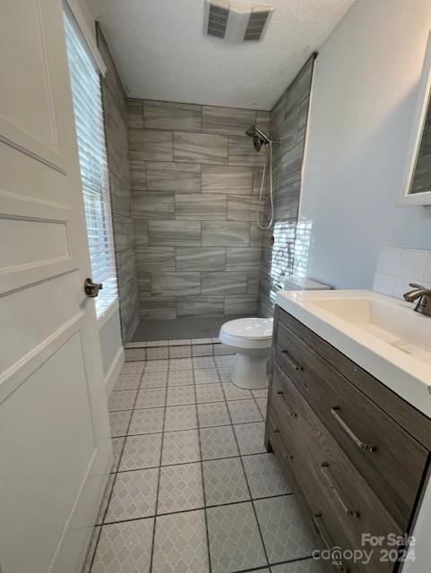 bathroom featuring vanity, a tile shower, tile patterned floors, and toilet