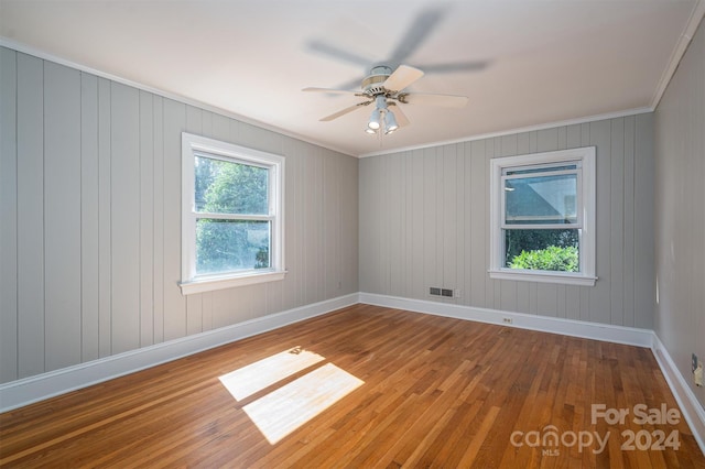 empty room with ornamental molding, ceiling fan, wood walls, and hardwood / wood-style floors