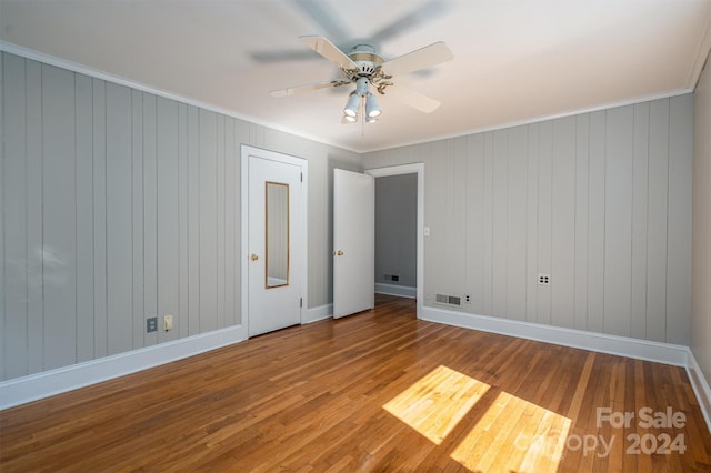 interior space with crown molding, ceiling fan, wood walls, and hardwood / wood-style floors