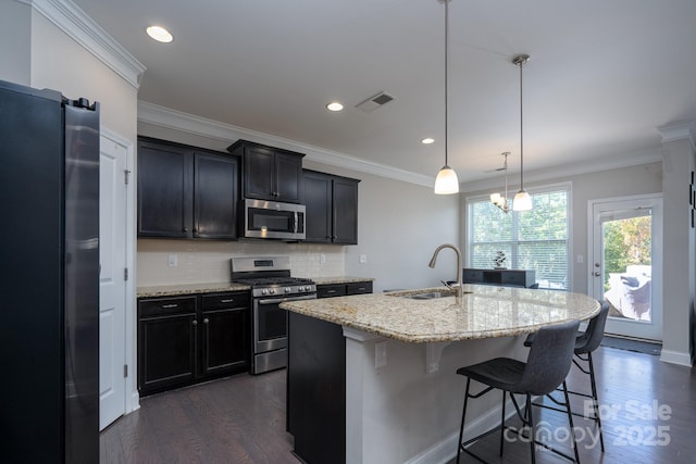 kitchen with sink, stainless steel appliances, light stone counters, an island with sink, and decorative light fixtures