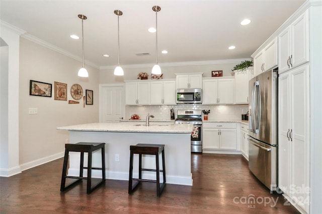 kitchen featuring dark wood-type flooring, a center island with sink, hanging light fixtures, appliances with stainless steel finishes, and white cabinetry