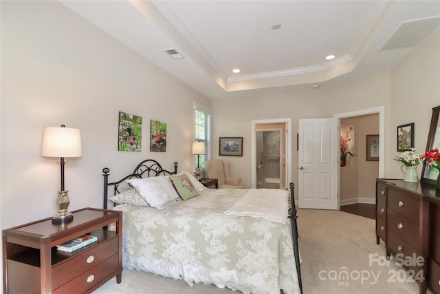 bedroom featuring ornamental molding, light carpet, a tray ceiling, and connected bathroom